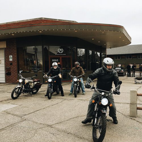 Motorcyclists in front of Janus building ready to ride.