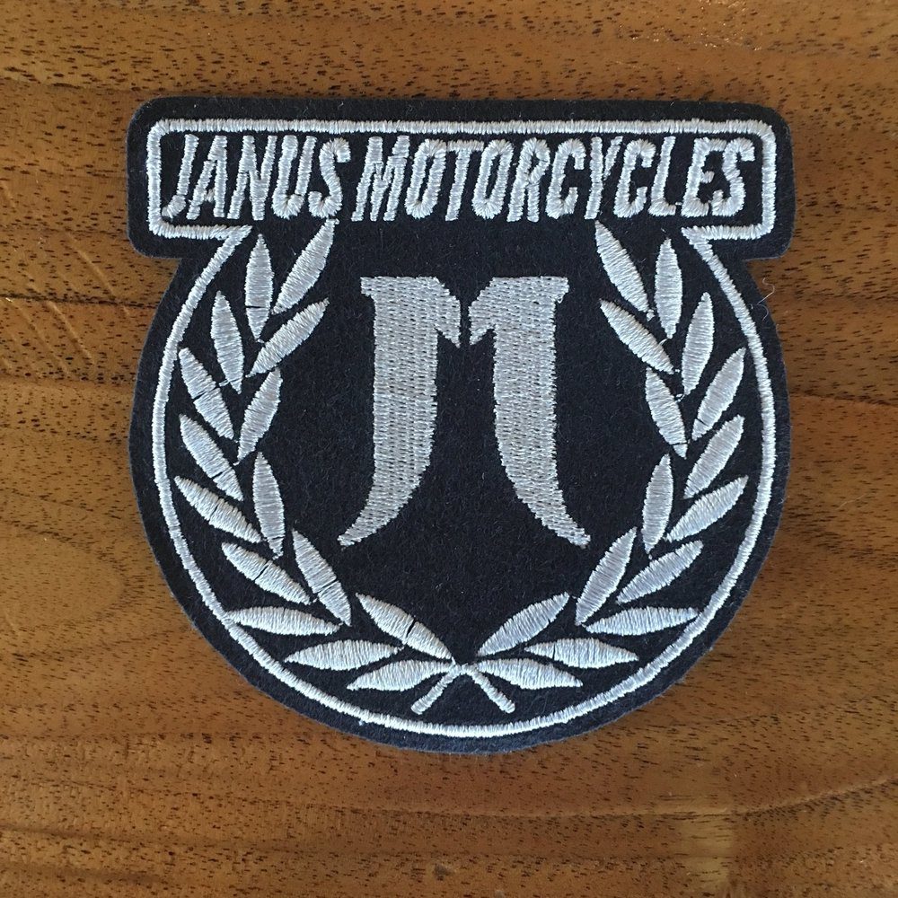 Janus Motorcycles patch with laurel wreath design on wooden surface.