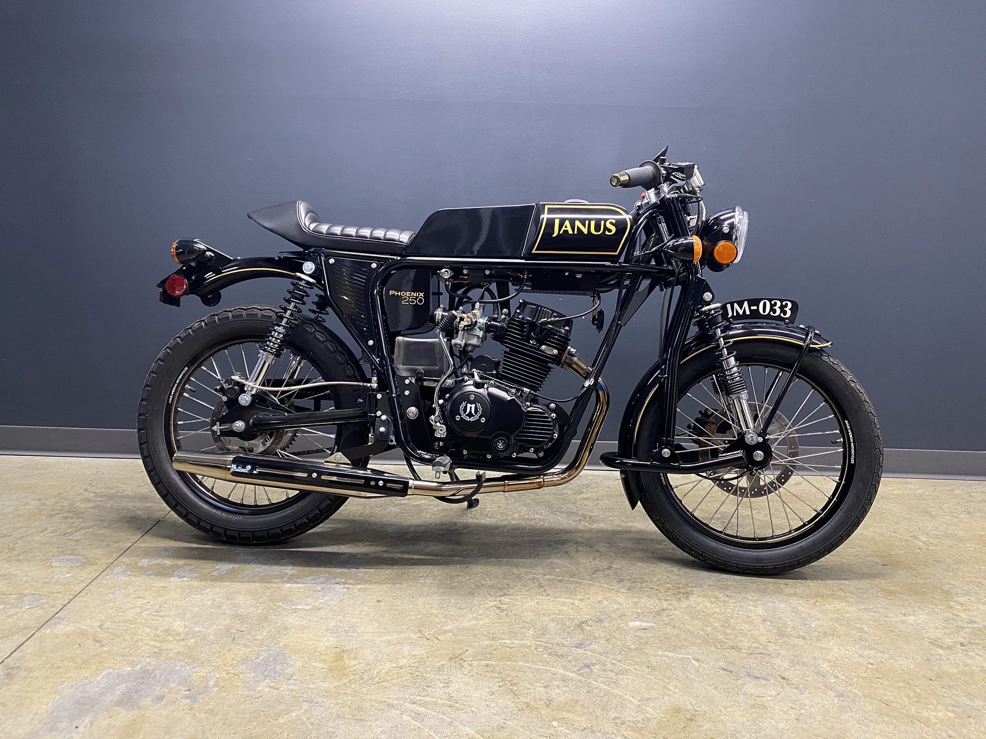 Black Janus motorcycle with gold detailing parked indoors.