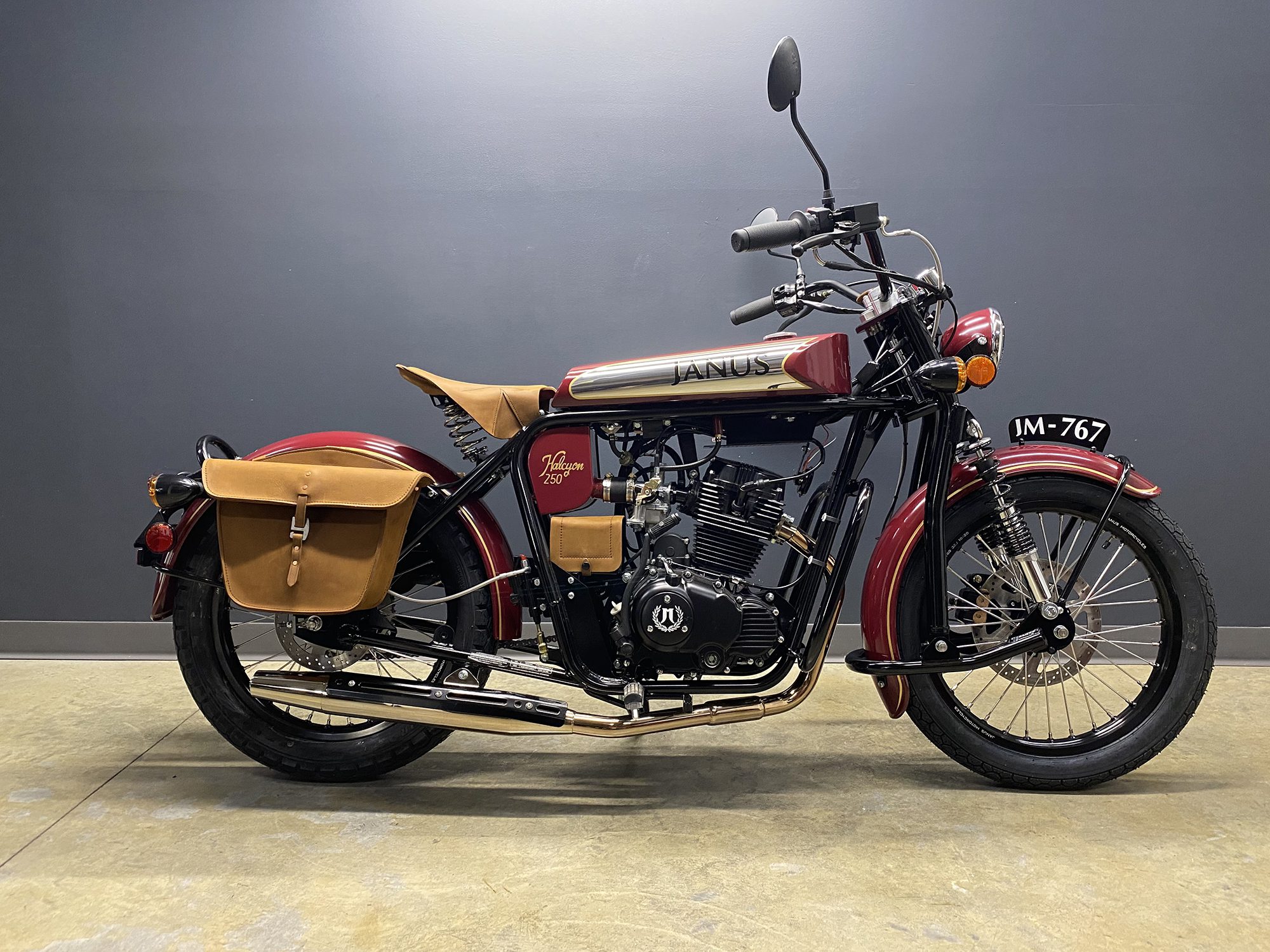 Classic maroon Janus motorcycle with tan saddlebags on display.