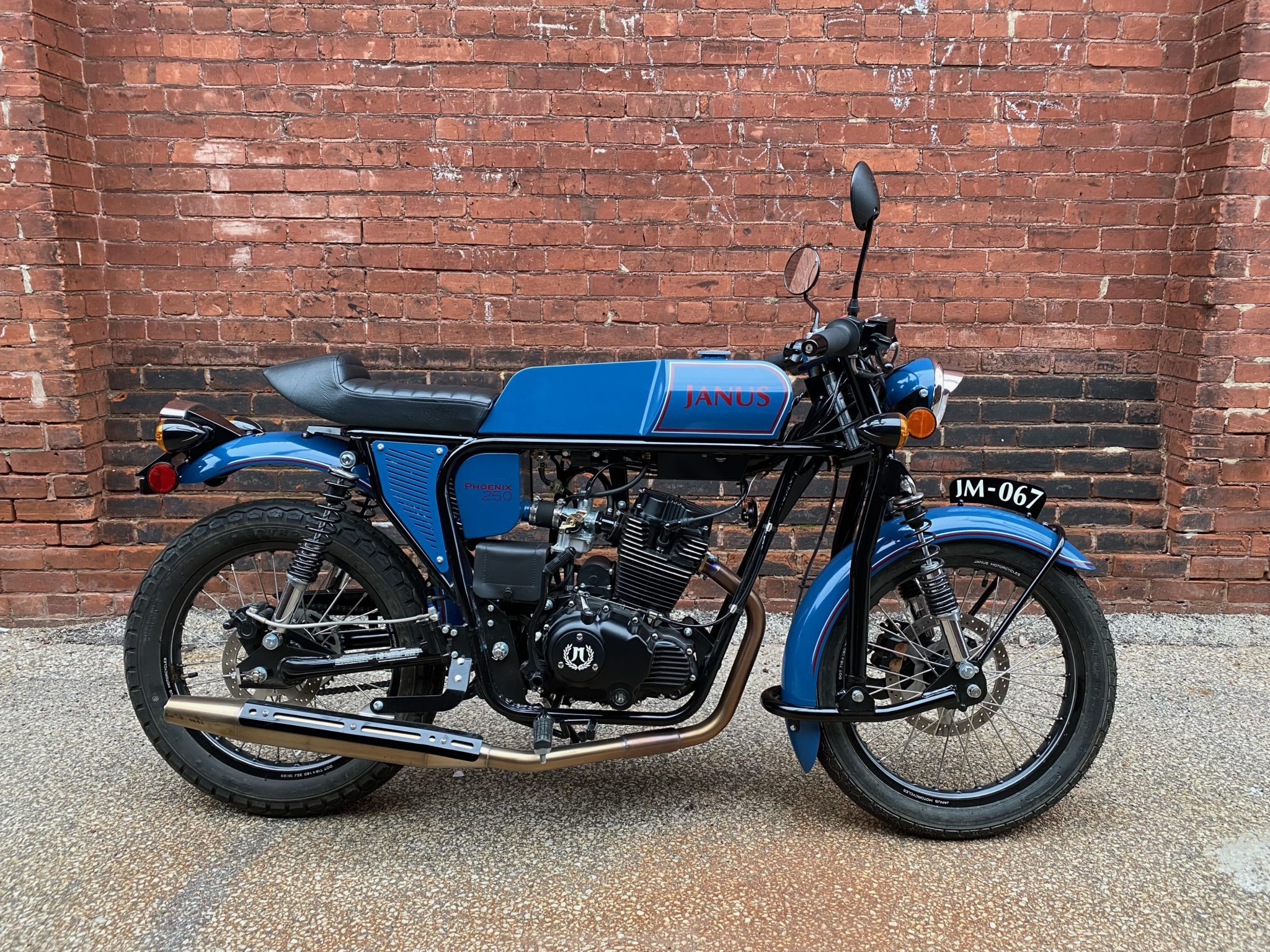 Blue Janus motorcycle parked in front of a brick wall.