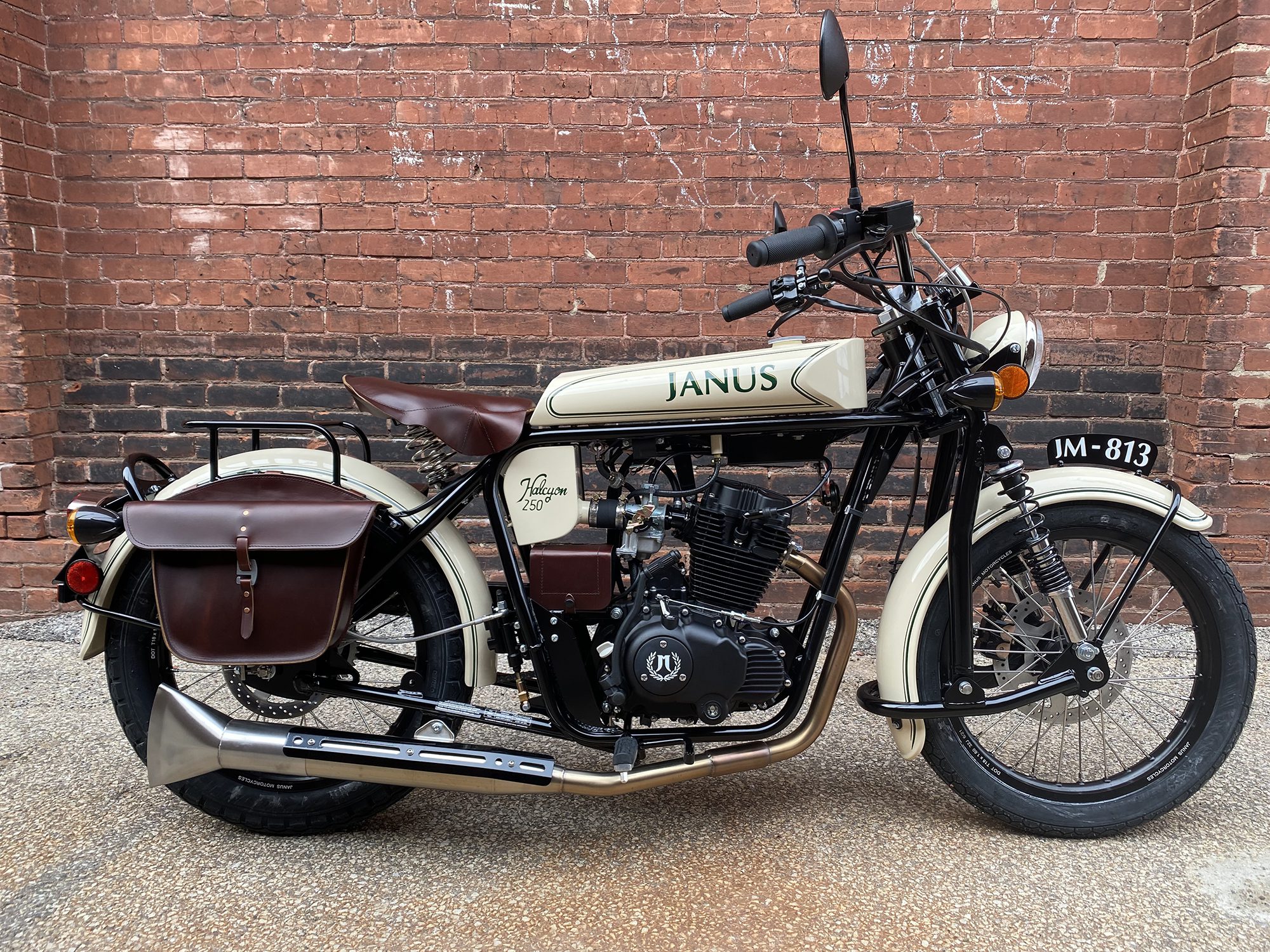 Vintage-style Janus motorcycle with side bags parked by a brick wall.