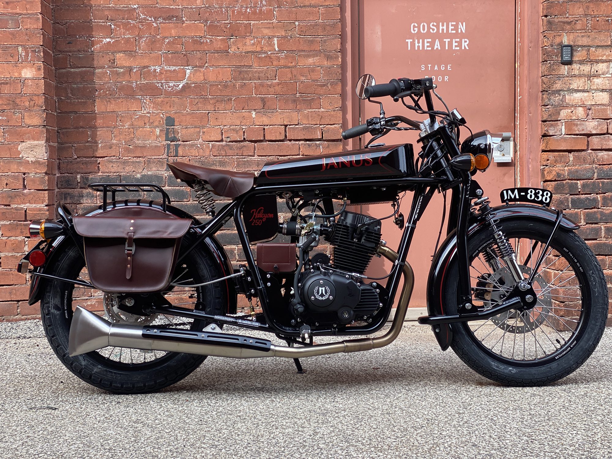 Classic black motorcycle parked against a brick wall near Goshen Theater entrance.